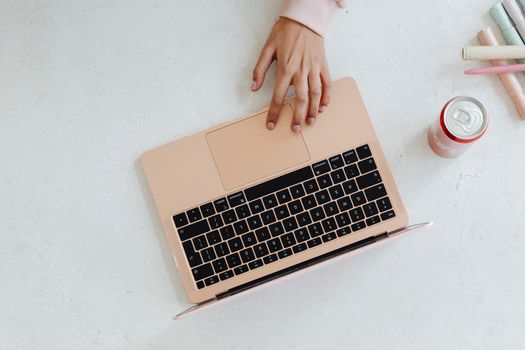 A person using a laptop on a white surface, next to a soda can and colored pencils.