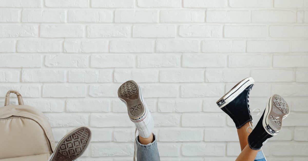 Three feet in sneakers raised against a stylish white brick wall, showcasing casual fashion and youthful vibe.