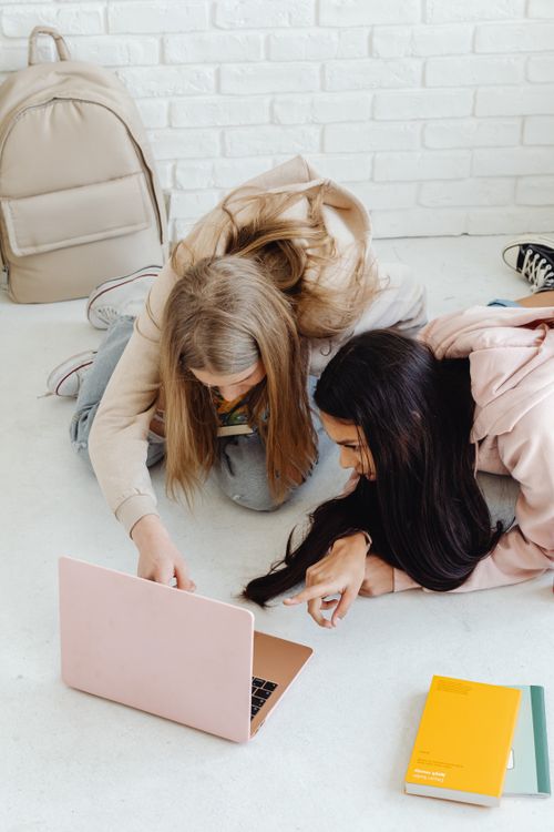 Free Two teenage girls studying with a laptop and books, discussing ideas indoors. Stock Photo