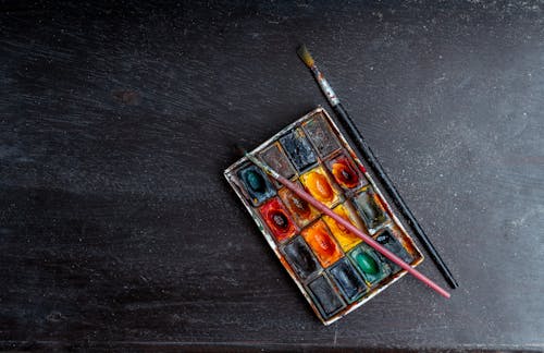 Top view of paintbrushes and set of watercolor paints placed on gray background