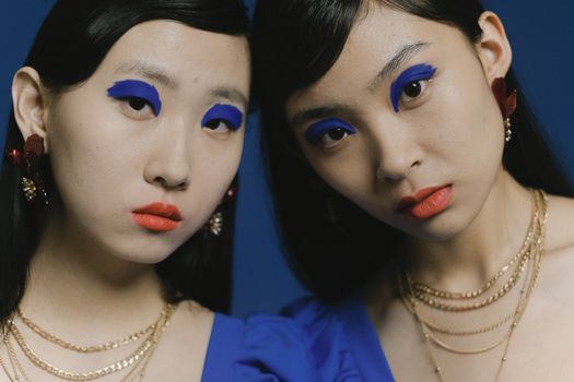 Eye-catching portrait of two women with vibrant blue eye makeup and gold jewelry.