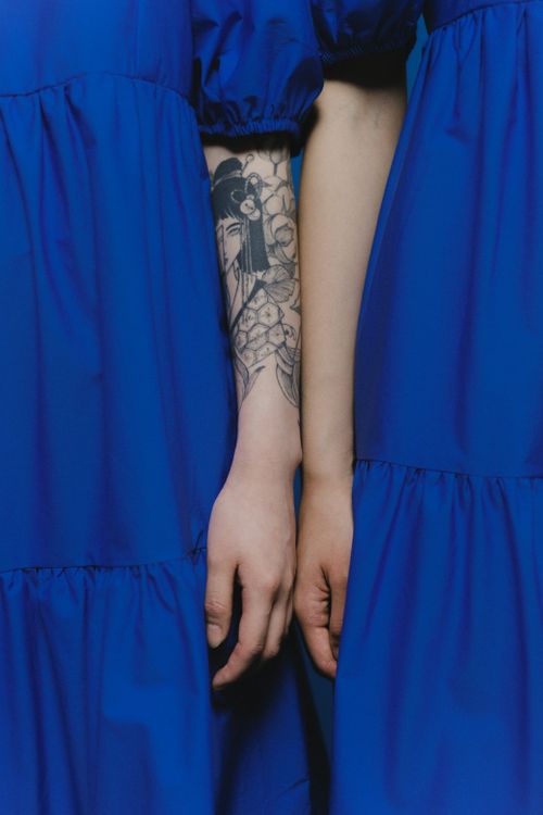 Free A stylish close-up of tattooed arms in matching blue dresses, showcasing art and fashion. Stock Photo