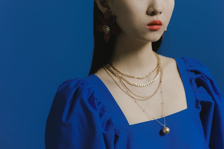 A Woman In Blue Shirt Wearing Gold Necklaces