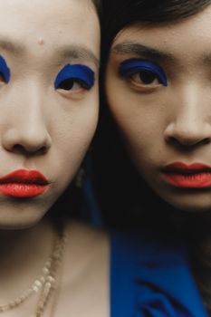 Creative close-up portrait of two women with vivid makeup and intense expressions.