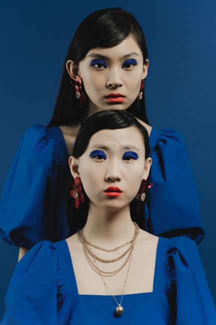 Stylish portrait of two Asian women in vibrant blue dresses with bold makeup and jewelry.