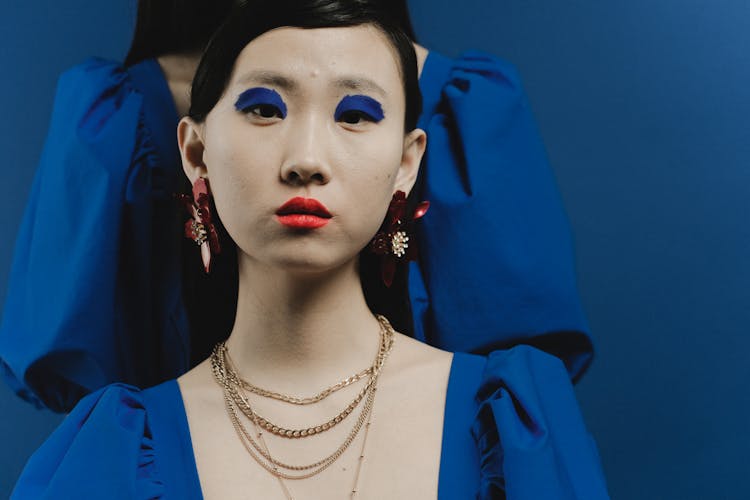 A Woman In Blue Shirt With Eyeshadow And Gold Necklaces