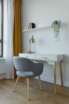 Stylish interior design featuring a gray armchair, white desk, and golden lamp.