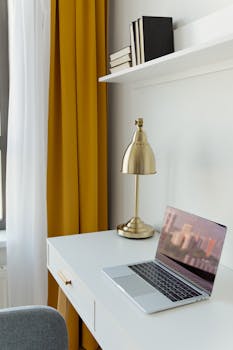 Stylish home office featuring a minimalist desk and a metallic lamp with bold yellow curtains for a contemporary look.