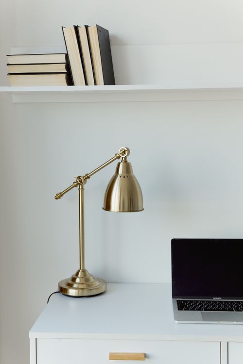 Free Stylish modern workspace with gold lamp, books, and laptop on a white desk. Perfect for minimalist interiors. Stock Photo