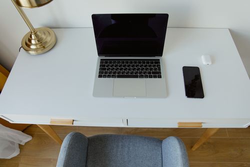 Free Stylish home office setup featuring a laptop, smartphone, and lamp on a minimalist white desk. Stock Photo