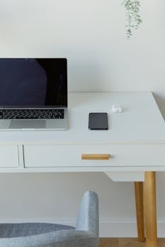 Minimalist white desk with laptop, smartphone, and earphones in a modern home office setup.