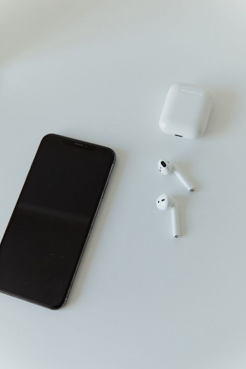 Black smartphone with wireless earbuds resting on a white table