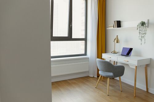 Free A bright, minimalist home office featuring a desk, chair, and window with yellow curtains and wooden floor. Stock Photo