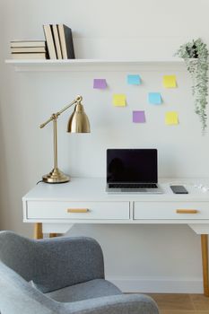 A sleek home office setup featuring a laptop, golden lamp, and sticky notes on a white desk with ample space.
