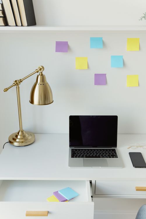 Free Organized desk space featuring a laptop, brass lamp, and colorful sticky notes for creative planning. Stock Photo