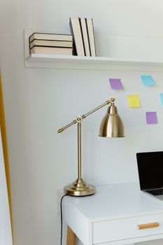 Elegant gold desk lamp on a minimalist white desk with books and sticky notes, perfect for modern office decor.