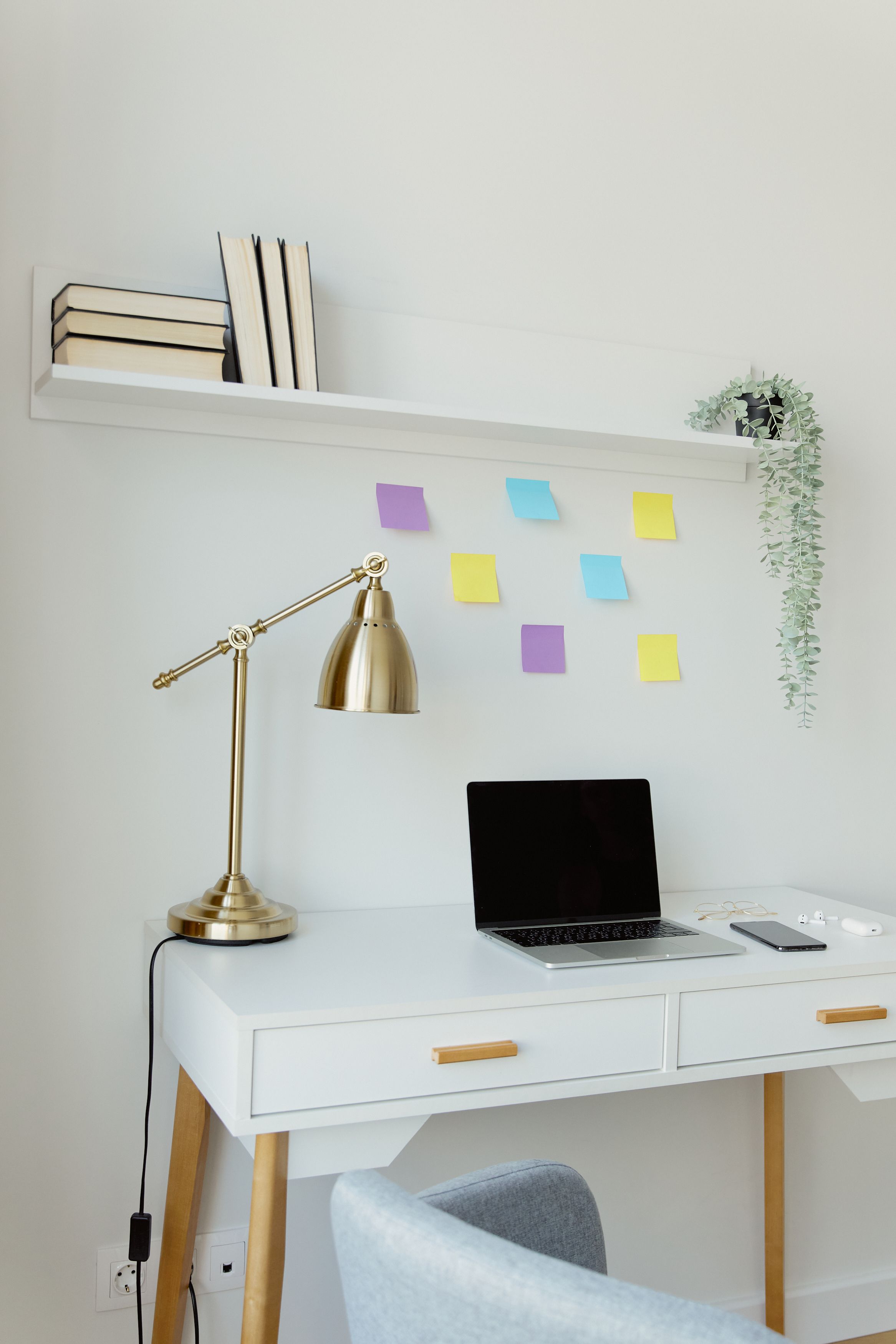 Mesa branca com notebook, luminária, livros e prateleira em home office organizado