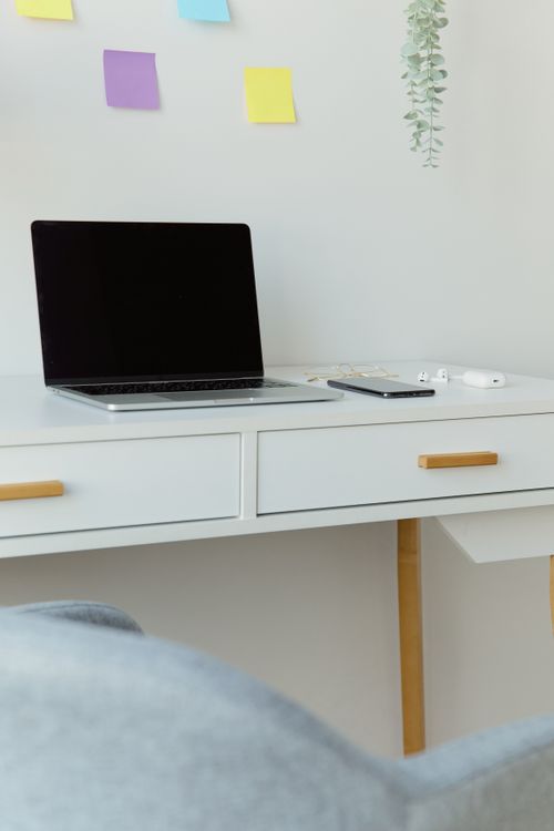 Free A minimalist home office setup with laptop, smartphone, and sticky notes on a white table. Stock Photo