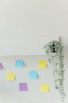 Vibrant sticky notes on a white wall with hanging plant, ideal for creative layouts.