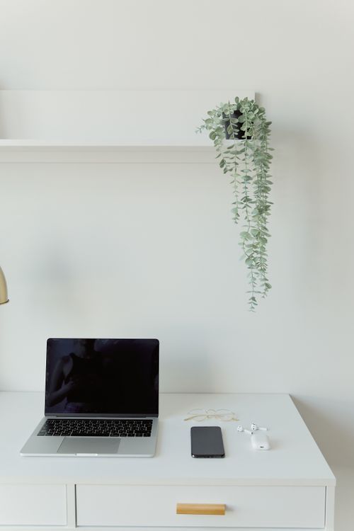 Free A clean, minimalist workspace featuring a laptop, smartphone, and houseplant on a white desk. Stock Photo
