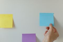 Hand placing colorful sticky notes on a minimalist white wall for home office organization.
