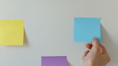 Hand placing colorful sticky notes on a minimalist white wall for home office organization.