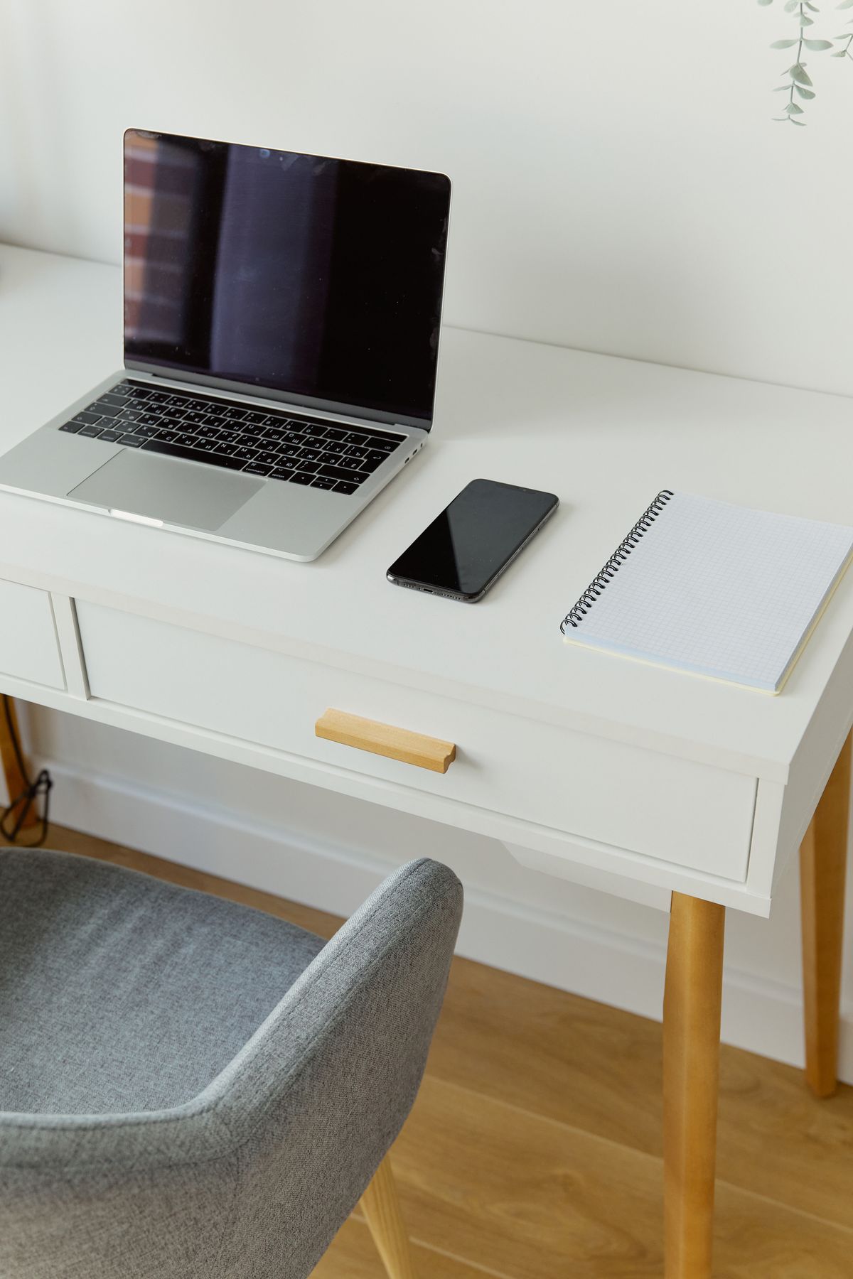 Minimalist professional desk with a silver laptop, smartphone, notebook, and subtle greenery