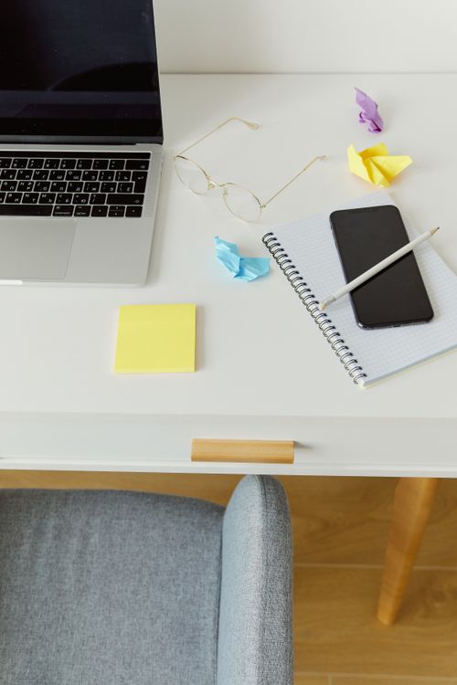 Free High-angle view of a minimalist desk with laptop, smartphone, notebook, and eyeglasses. Stock Photo