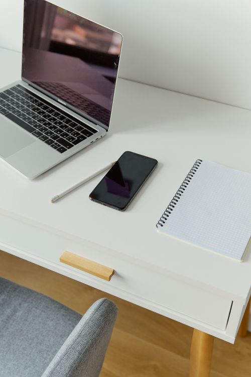Free A sleek workspace featuring a laptop, smartphone, and notebook on a white table. Stock Photo