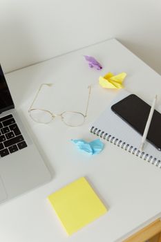 Organized office desk with laptop, glasses, and colorful paper for creative work.