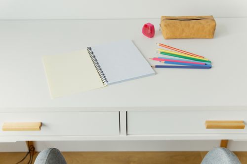 Free An organized workspace featuring a notebook with colored pencils and stationery on a white table. Stock Photo