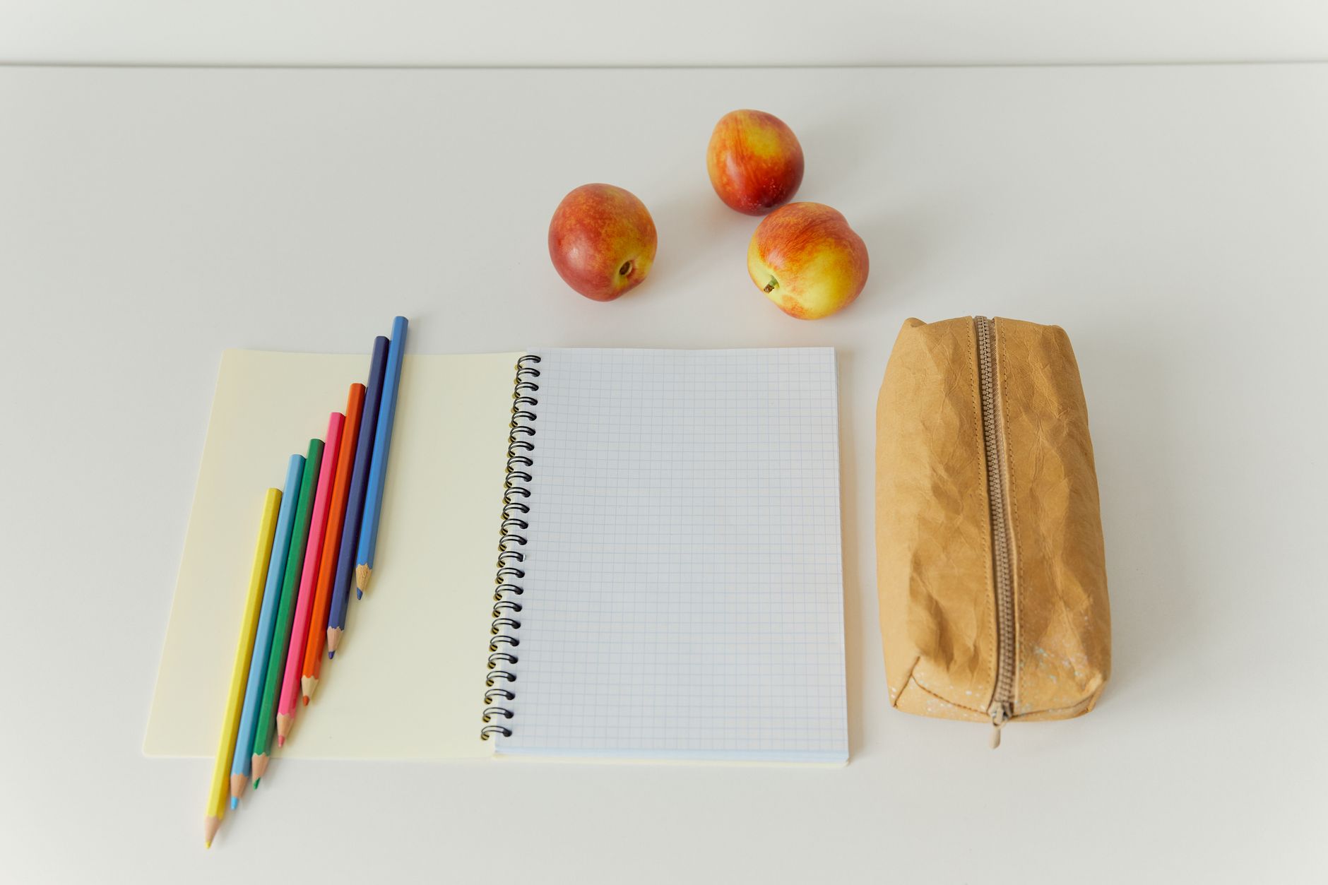 Artistic workspace with colored pencils, apples, and a notebook on a table.