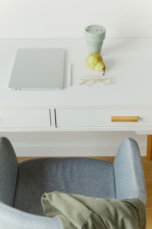 Free A clean and minimalist workspace with a laptop, pear, and reusable cup on a white desk. Stock Photo