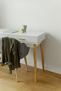 Minimalist workspace featuring a wooden desk and chair with a cup and laptop in a well-lit room.
