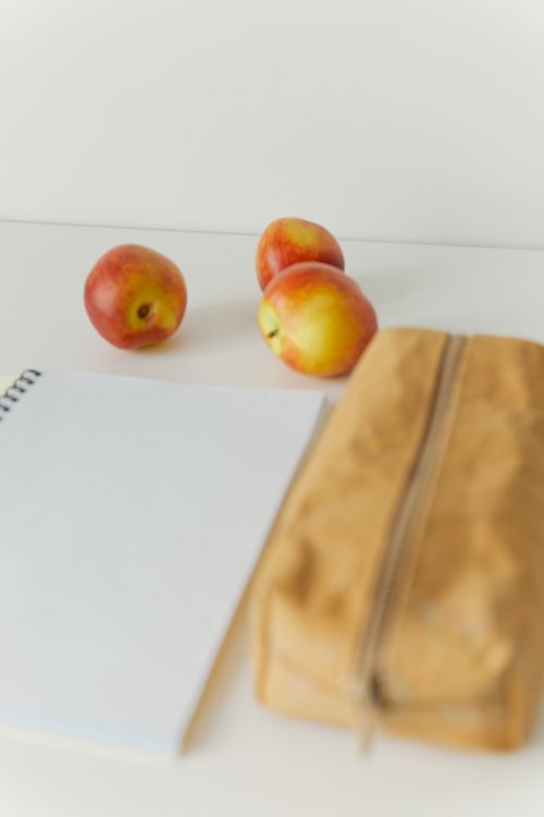 Free A clean and simple workspace featuring red apples, a notebook, and a pencil case on a table. Stock Photo