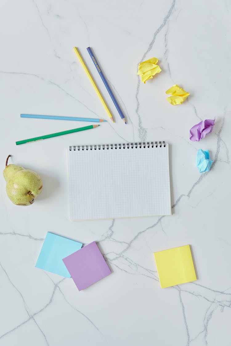 Colorful Stationeries And Pear On A White Surface