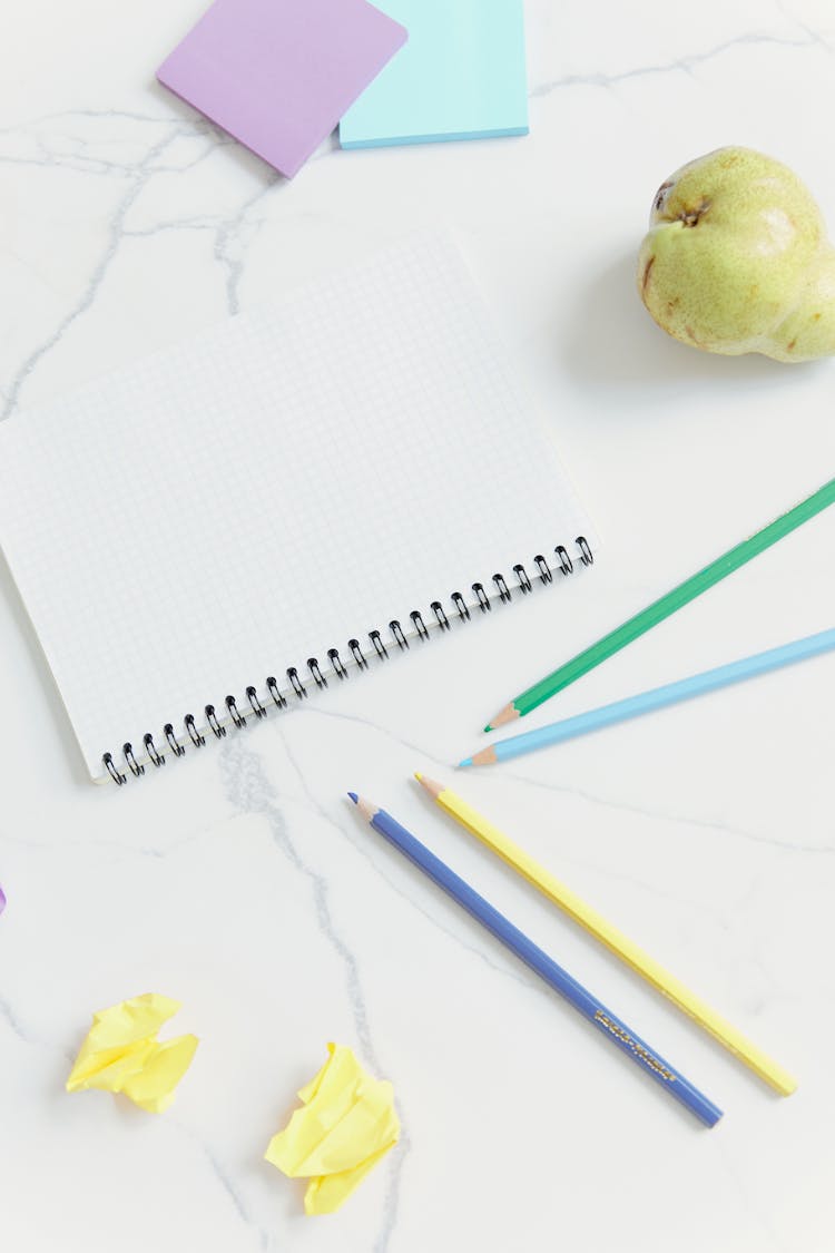 Colorful Stationeries And Pear Fruit On A White Surface