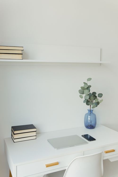 Free A minimalist white workspace featuring a laptop, phone, books, and a vase with eucalyptus on a white desk. Stock Photo