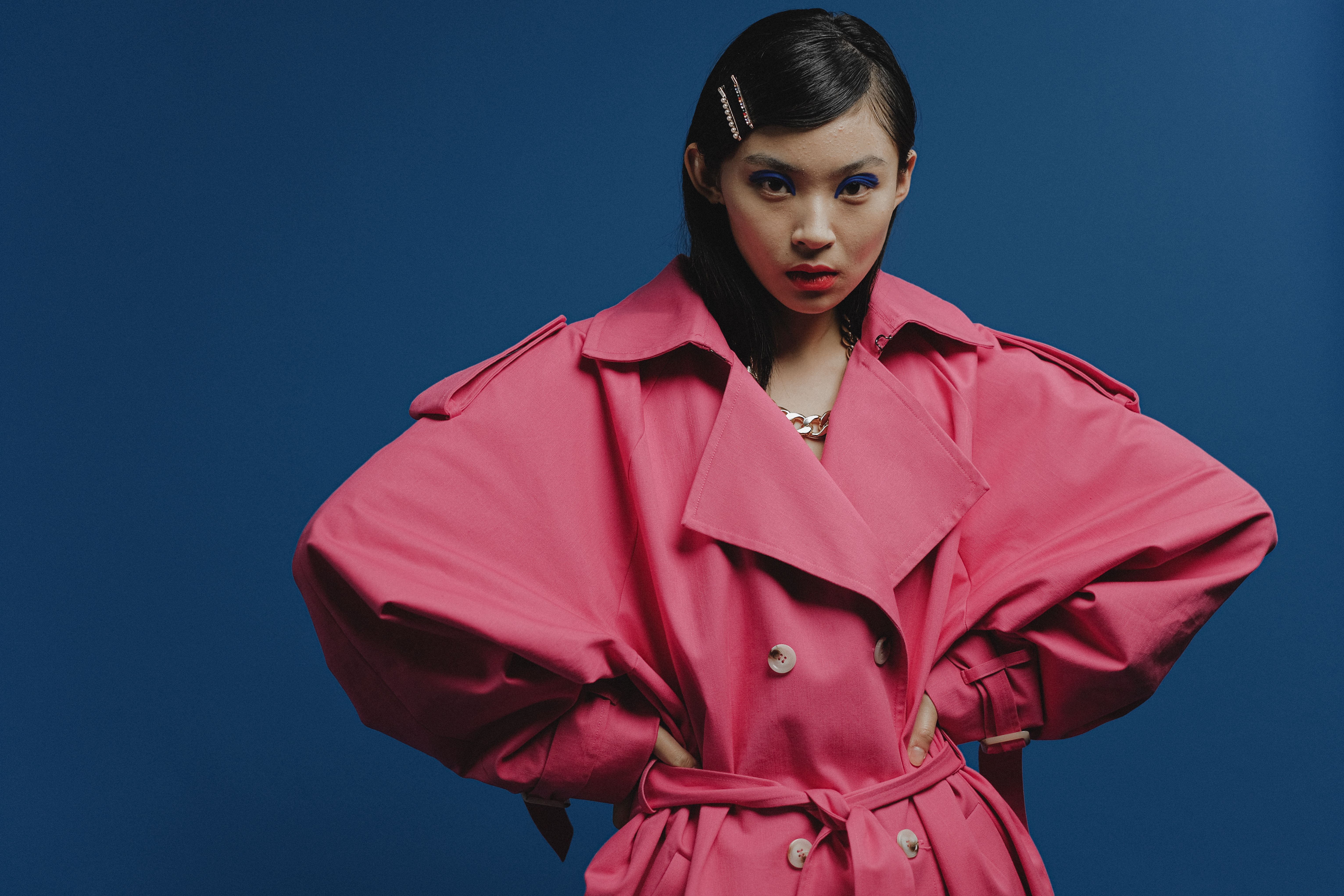 Stylish woman posing in pink coat against blue background, studio shot.