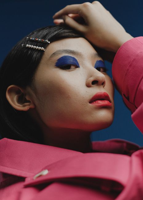 Close-up of a woman with bold eye shadow and red lips, striking a confident pose.