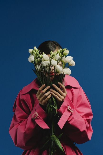 Woman in a pink coat holds white roses against a blue background.