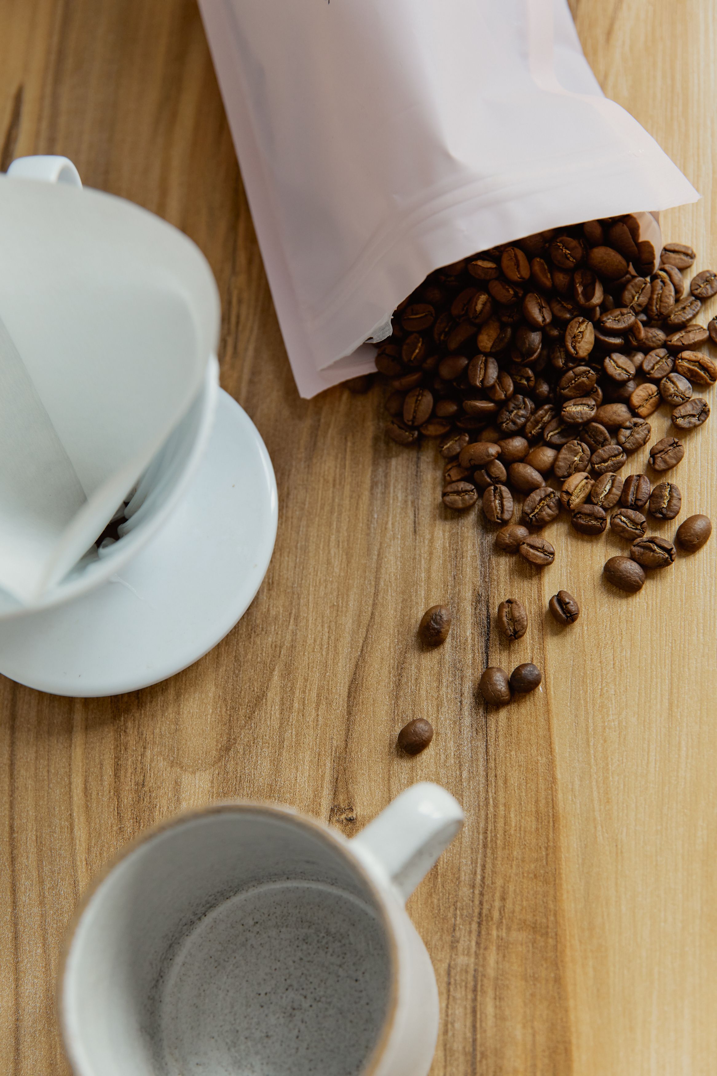 Roasted coffee beans beside a handmade ceramic mug on a wooden table