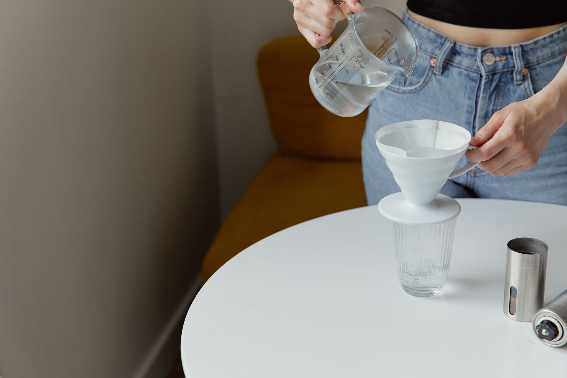 A person preparing pour-over coffee with a glass kettle and paper filter indoors.