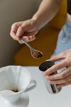 Close-up of hand preparing coffee with a spoonful of ground coffee.