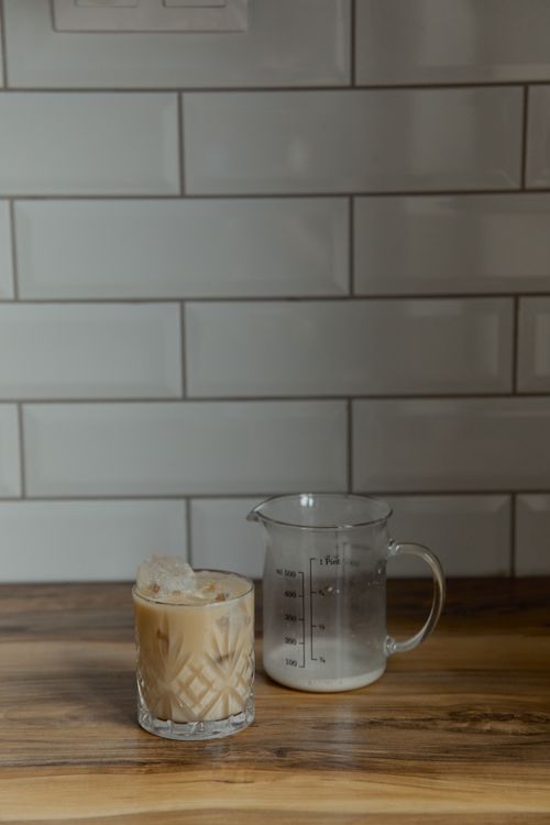 Free A refreshing glass of iced coffee next to a measuring cup on a wooden countertop in soft lighting. Stock Photo