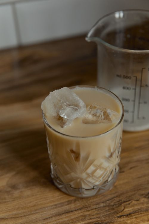 Free A delicious iced coffee in a glass with ice cubes on a wooden table next to a measuring cup. Stock Photo
