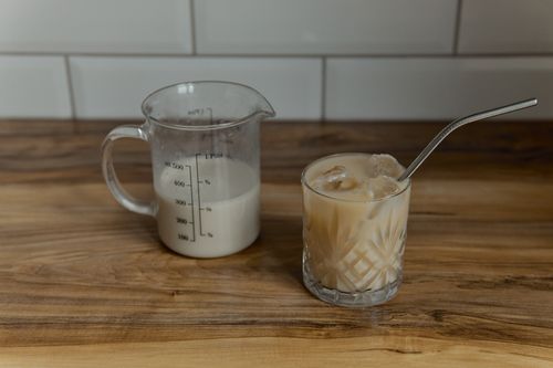Free Iced coffee latte in crystal glass with metal straw next to measuring cup on wooden surface. Stock Photo