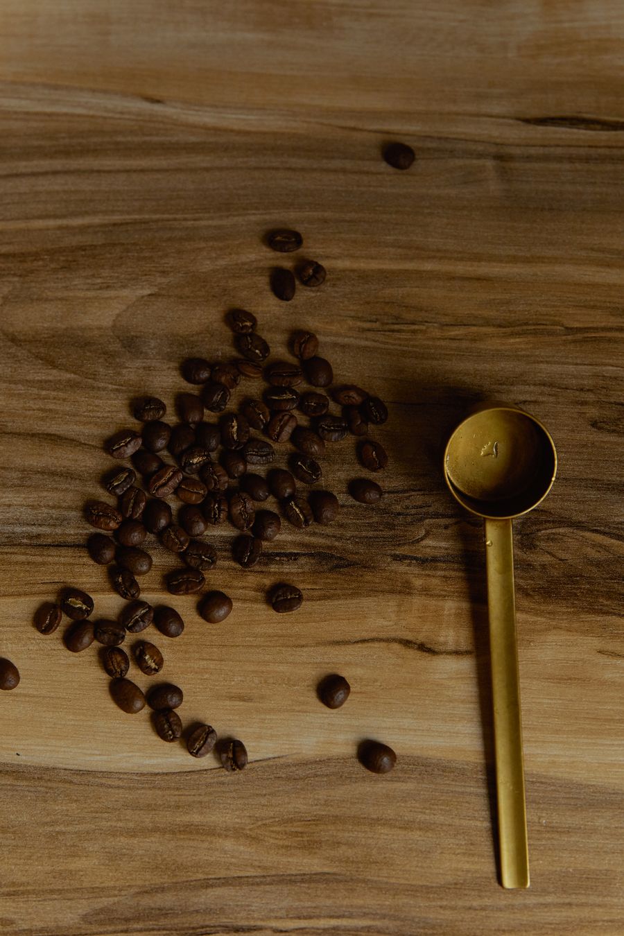 Coffee beans and a brass spoon scattered on rustic wood — photo by Darina Belonogova on Pexels