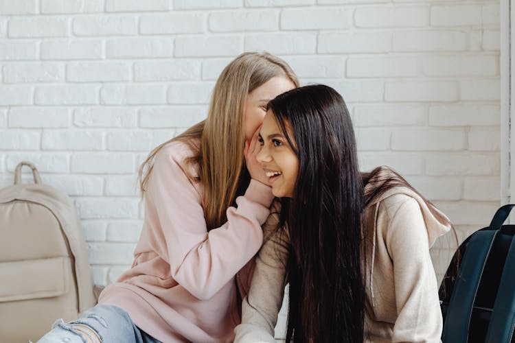 Young Women Whispering To The Women Sitting Next To Her