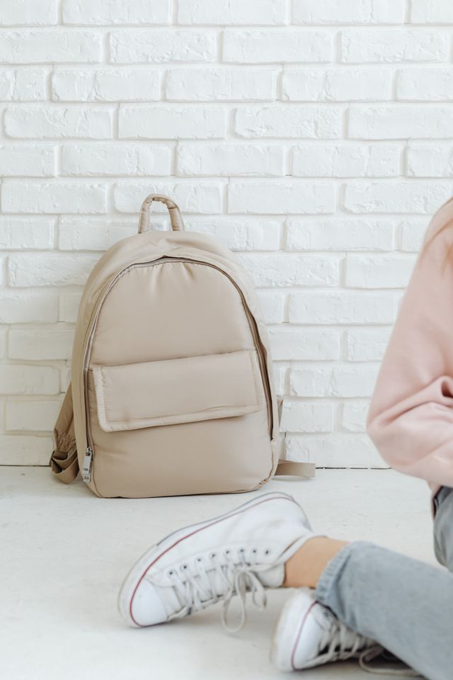 A beige canvas backpack resting against a white wall